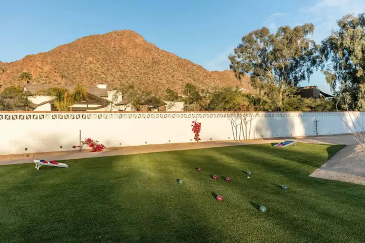 A scenic exterior image capturing a mountain backdrop, landscaped garden, and families enjoying lawn games at sunset. The relaxed mood and wide open space invite playful outdoor gatherings against a stunning natural backdrop.