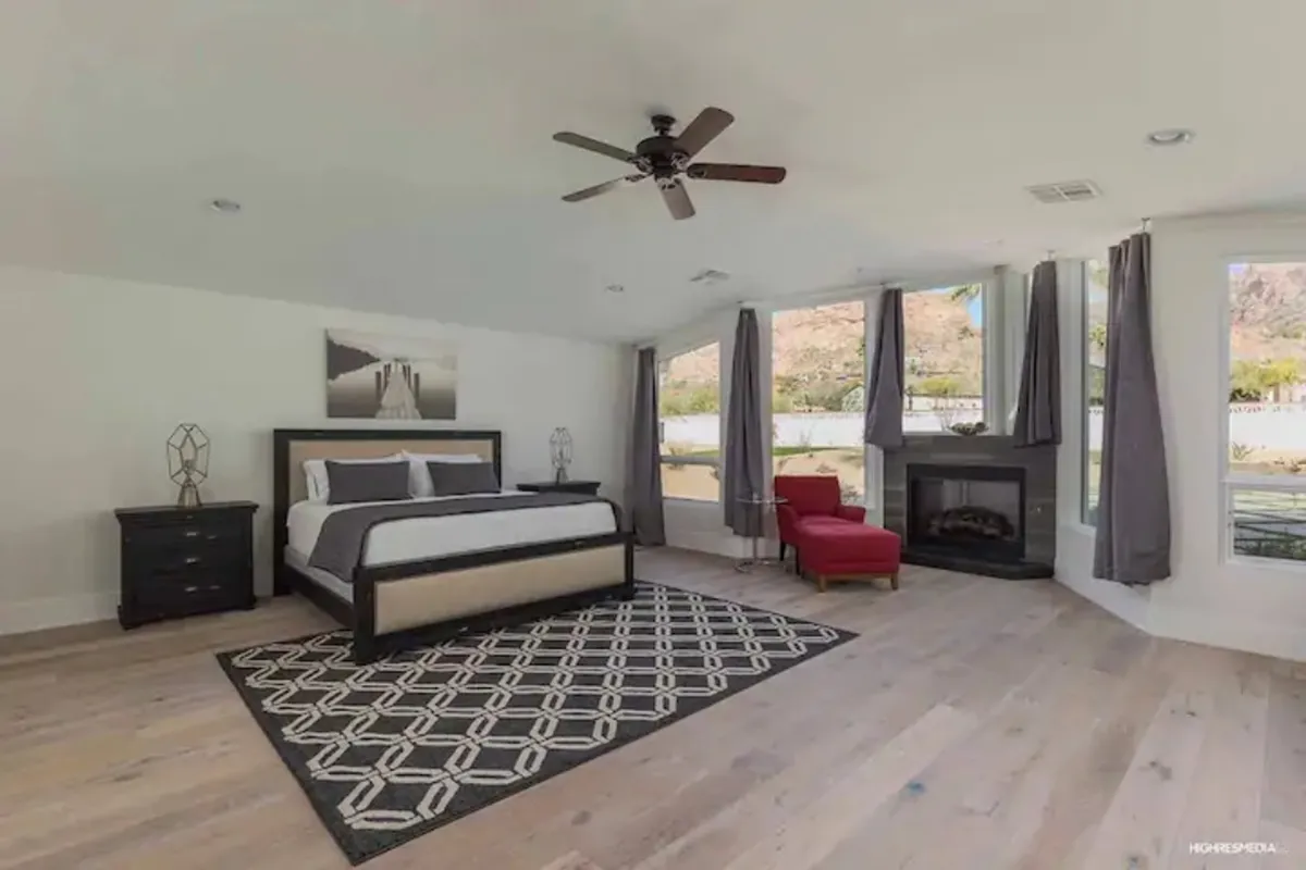 A tranquil bedroom featuring a plush bed with crisp linens, a cozy fireplace, an armchair for reading, and large windows that let in natural light. The soft rug and tasteful decor create a restful ambiance.