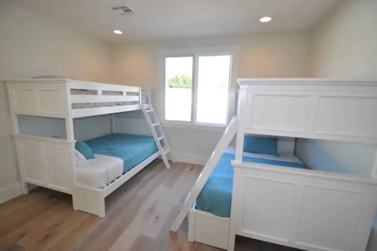 A cheerful bedroom fitted with bunk beds, light-colored walls, and expansive windows that flood the space with sunlight. The playful arrangement creates a welcoming space for families or groups, emphasizing flexible sleeping options.