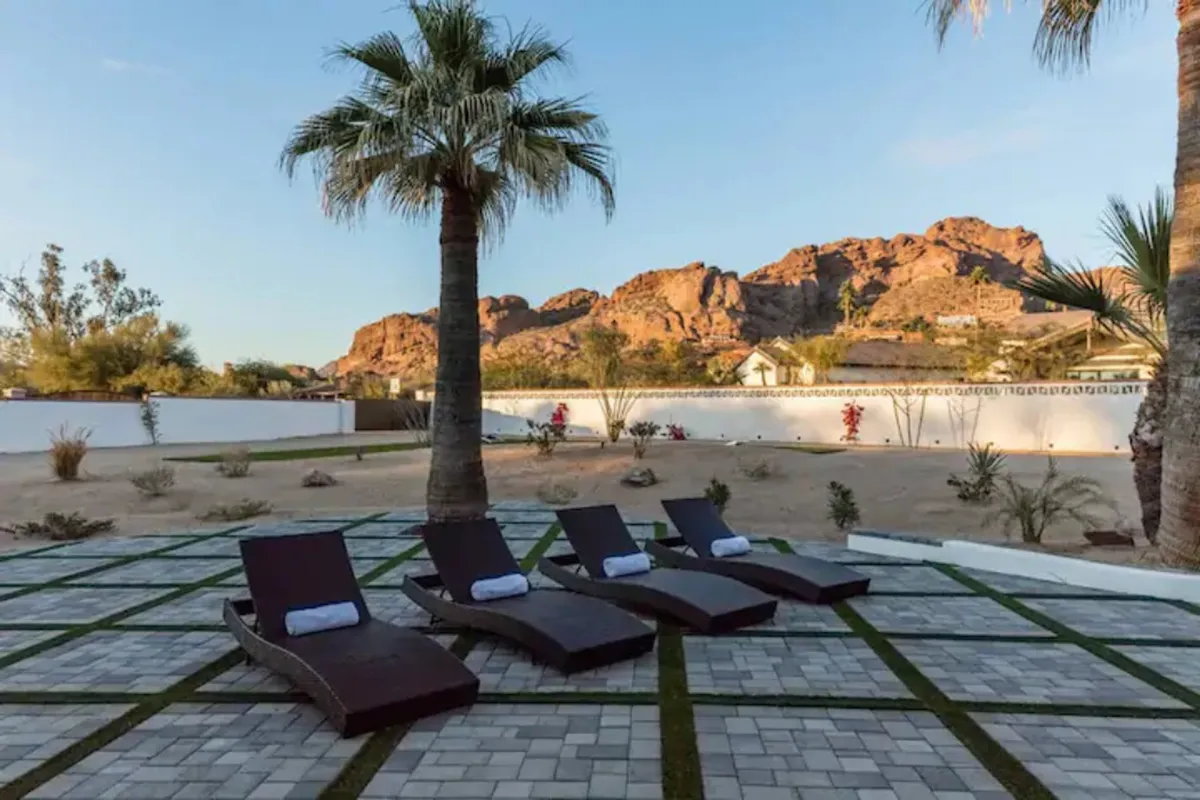 An inviting backyard scene featuring palm trees, lounge chairs, and a relaxing seating area, all set against the backdrop of colorful mountains at sunset. The space radiates tranquility and is ideal for unwinding after a day outdoors.