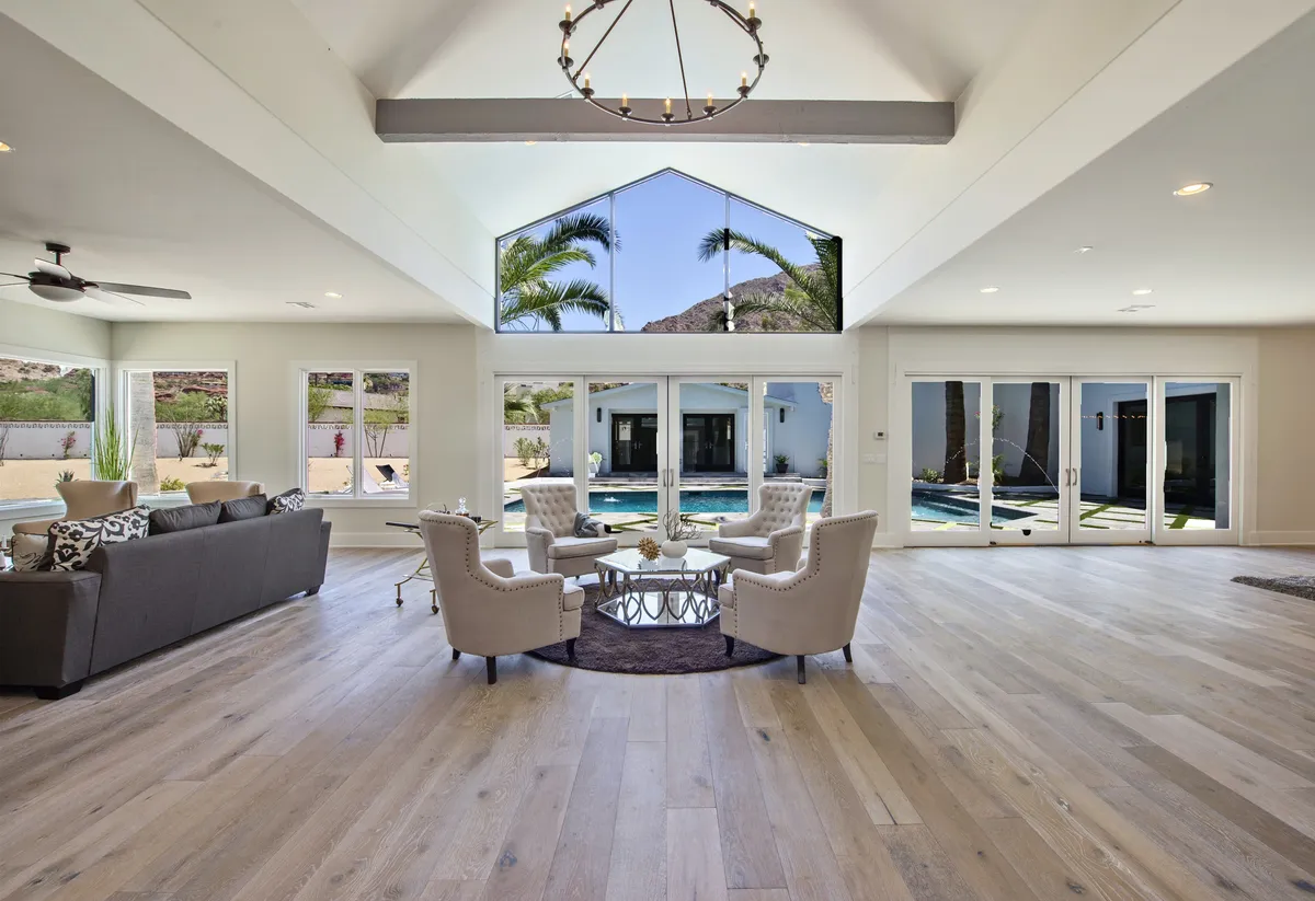 A spacious, sun-drenched living area featuring expansive glass windows that frame stunning views of Camelback Mountain. The room is arranged with plush, modern seating and a chic coffee table, creating an inviting space for social gatherings and relaxed afternoons.