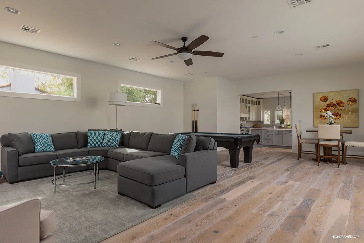 An open-plan living and dining area that seamlessly combines a comfortable sectional sofa, a stylish coffee table, a pool table, and a dining table, all within view of large windows. The artwork and decor add warmth, making it ideal for entertaining and group activities.