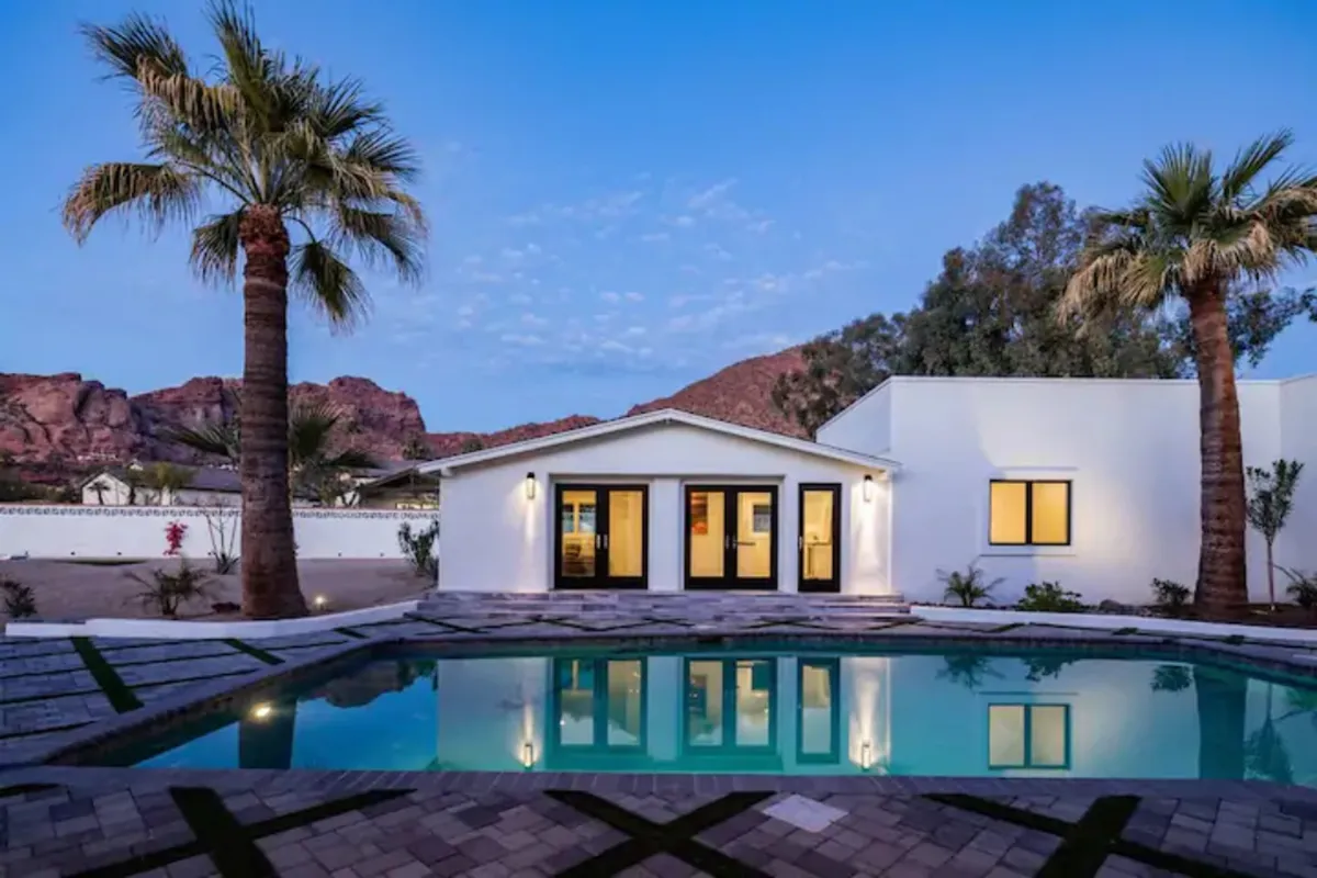 A broad view of a sparkling swimming pool with palm trees, the house facade, and Camelback Mountain as a stunning backdrop. The space is designed for sunbathing, swimming, or taking in the majestic views—embodying the Arizona resort lifestyle.