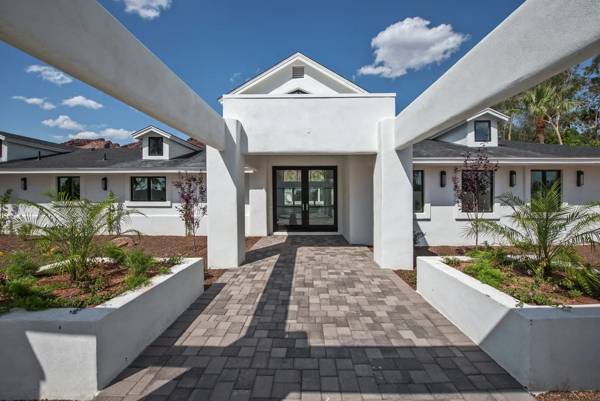 The image shows the inviting entranceway of a luxury estate, framed by manicured landscaping and a welcoming pathway. Warm lighting and lush greenery create a sophisticated, private ambiance ideal for executive retreats.