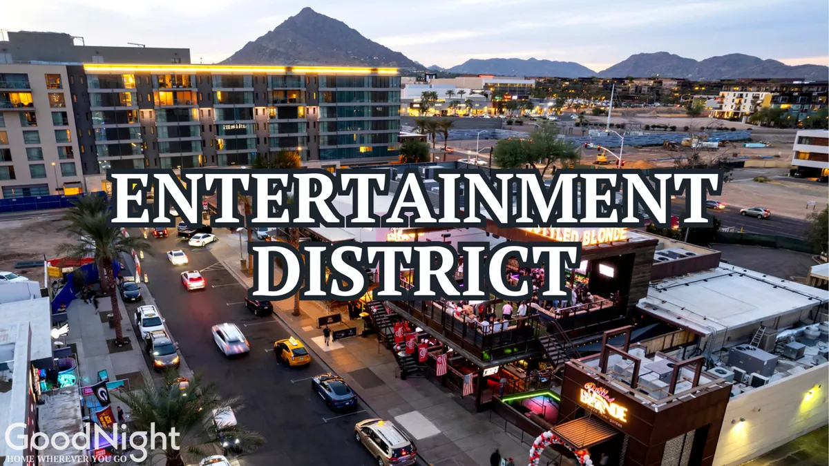 The image depicts a lively entertainment district with an illuminated sign, outdoor seating areas bustling with activity, and parked cars lining the street. The scene is set in the evening, hinting at vibrant nightlife, dining, and social opportunities just minutes away.
